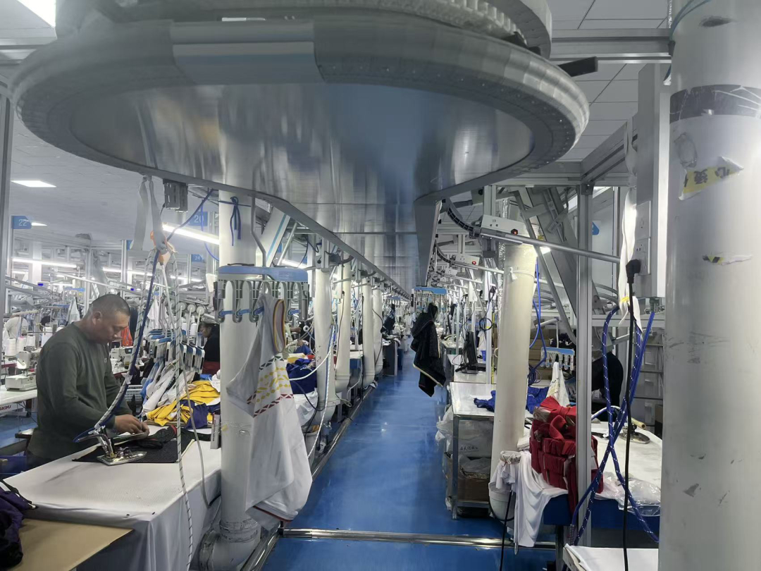 Overhead garment conveyor system carrying garments between sewing stations on the production floor
